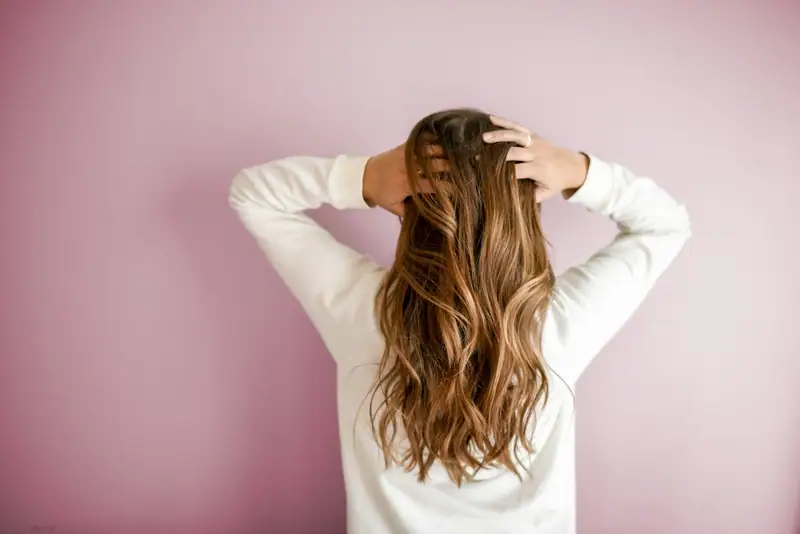 Long caramel hair, hands raised, pink wall