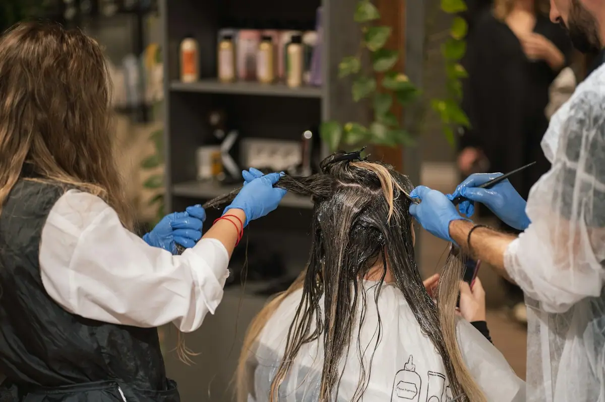 Colourist applying colour to hair with gloved hands in a salon