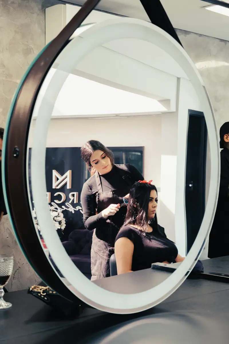 Round lit salon mirror reflecting a stylist and client