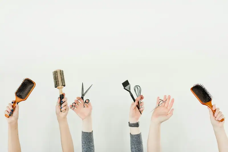 Hands holding brushes, scissors and a tinting brush against a white wall